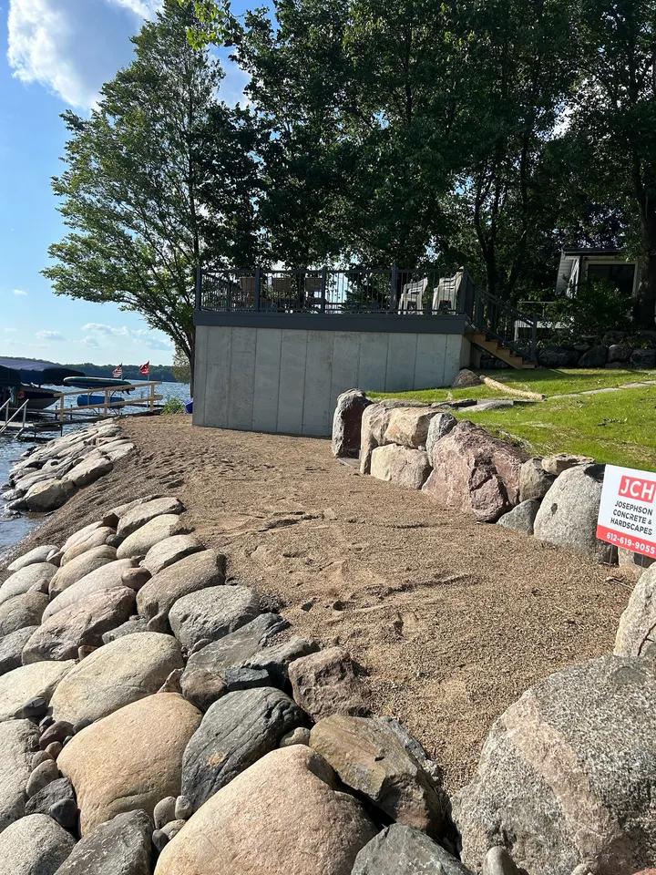 Freshly placed boulder riprap along a lake shoreline with a graded bank and a small lake shed above it