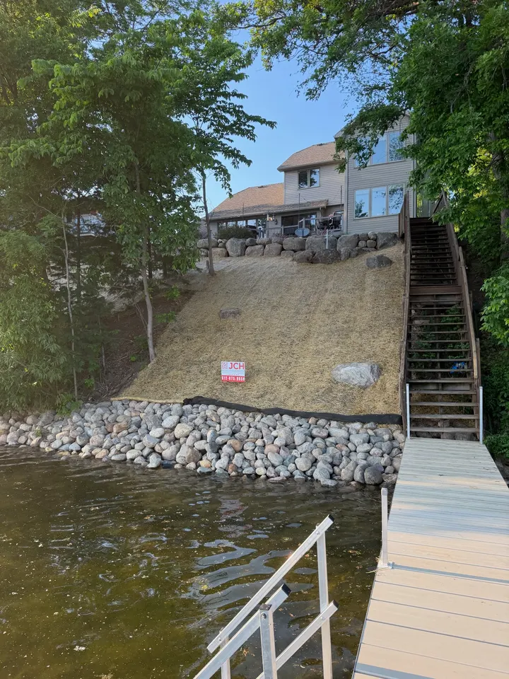 Riprap shoreline along a lake with a long stairway up a seeded bank to a house