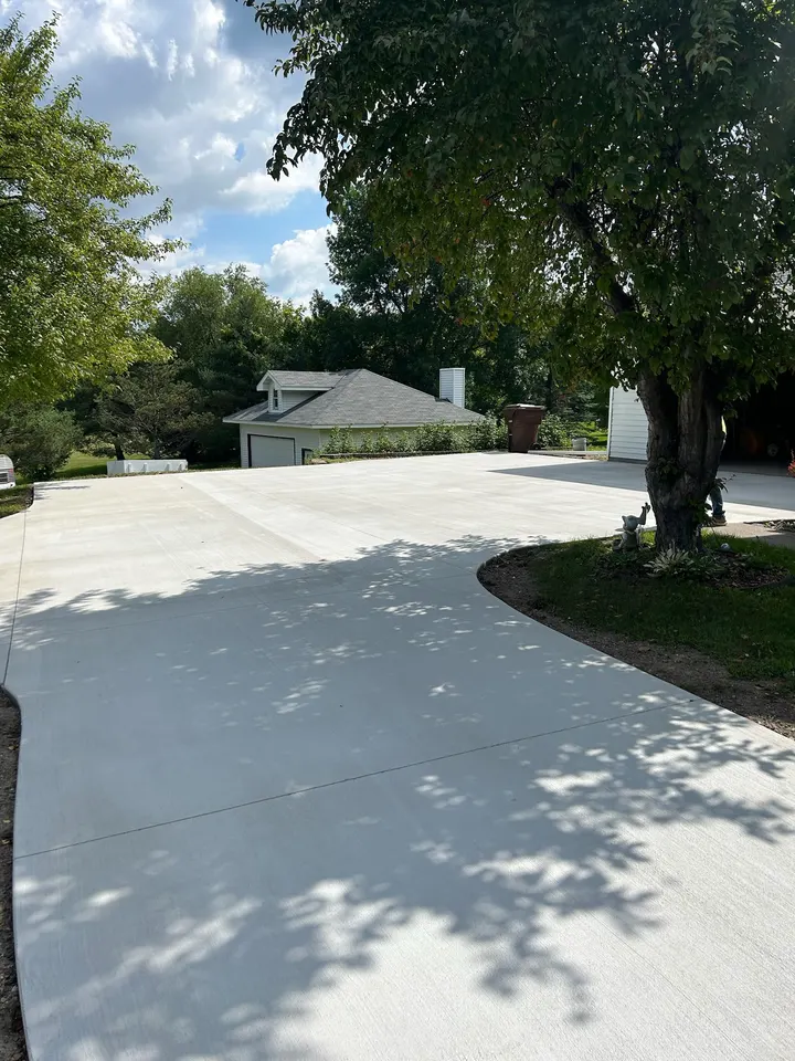Wide broom-finish concrete driveway under mature shade trees, curving toward the street