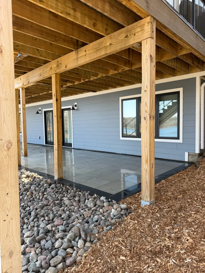 Finished concrete slab under a timber-framed deck with river rock at the edge