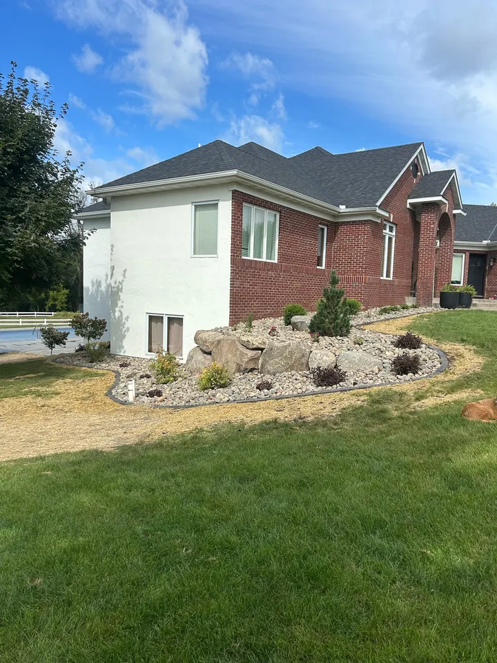 River rock beds with boulders and shrubs along the side of a brick and stucco home