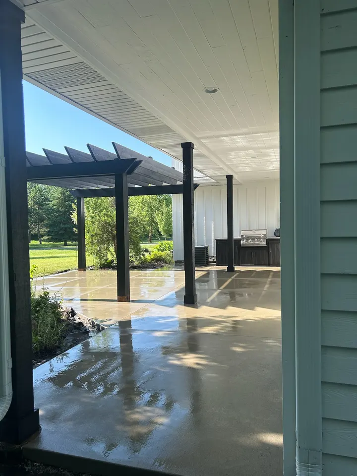 Sealed concrete floor under a covered patio with black posts, looking out to a lawn and trees