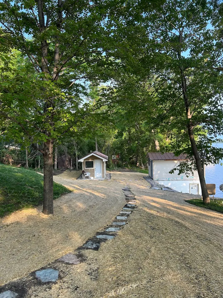 Curved stepping stone path running down a freshly seeded slope past a small shed toward a boathouse at the lake edge